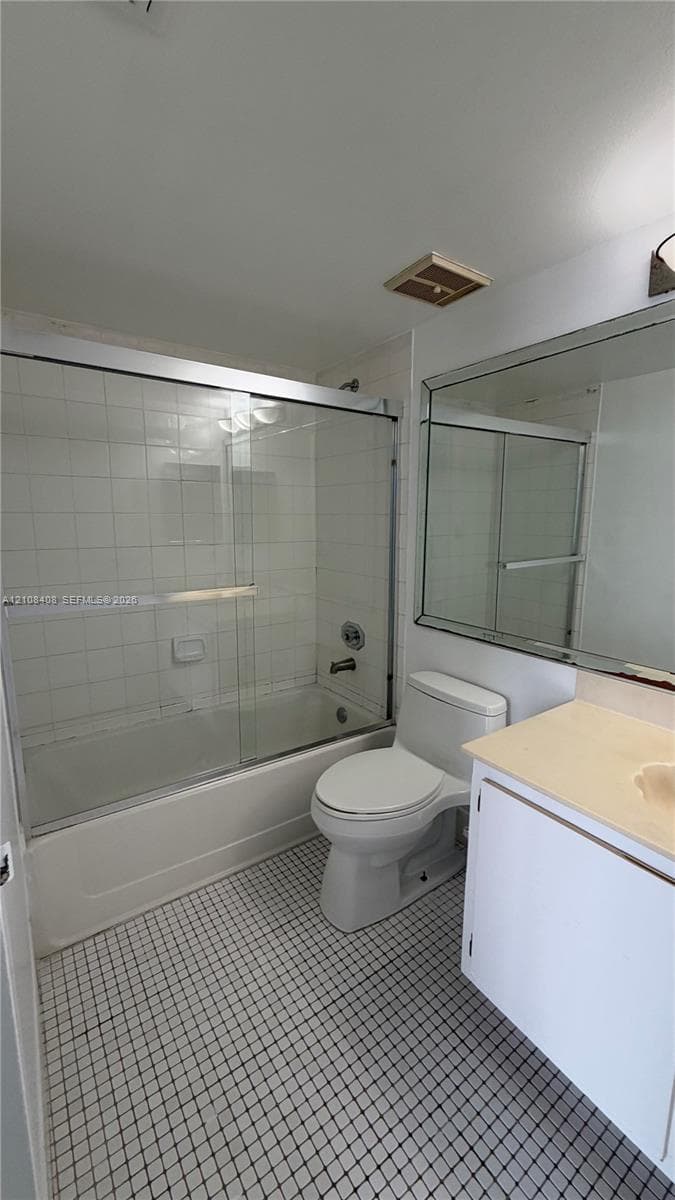 Bathroom featuring a combination bathtub and shower with a glass sliding enclosure, white tiled tub surround, vanity with a solid-surface countertop, and a large wall-mounted mirror