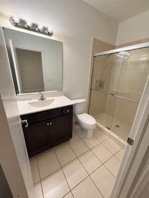 Dark wood-finish vanity with a rectangular sink and solid-surface countertop, four-light vanity fixture, large wall-mounted mirror, ceramic tile flooring, and glass-enclosed shower with decorative tile inlay