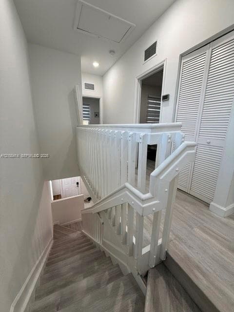Staircase featuring a white wood balustrade and handrail, paired with light-toned wood-finish flooring and louvered bifold closet doors
