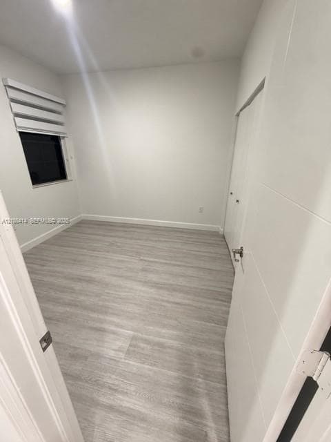 Interior space featuring light-toned wood-finish flooring, neutral wall paint, a single window with installed roller shades, and a closet with double-panel doors