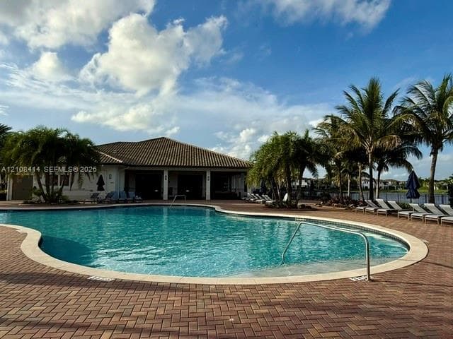 Community pool featuring a curved concrete deck, paver-stone surround, metal handrails, and surrounding palm trees