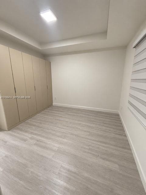 Neutral-toned room featuring a tray ceiling, integrated wall-to-wall cabinetry, wood-finish flooring, and a multi-layered window shade