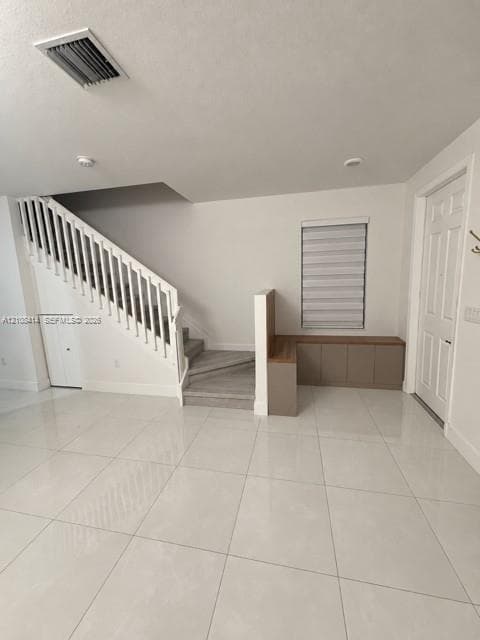 Staircase with white balusters and wood-finish treads, large-format tile flooring, built-in cabinetry with a wood-finish surface, and a single-panel interior door