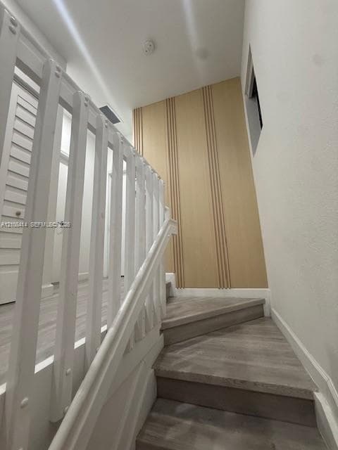Staircase featuring wood-finish flooring, white railing with vertical balusters, and a decorative wood-slat accent wall