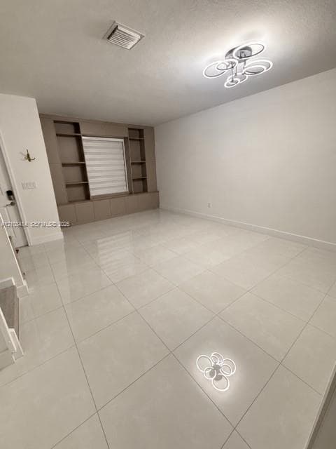 Large-format tile flooring, custom built-in cabinetry with integrated shelving, and a modern multi-ring flush-mount light fixture