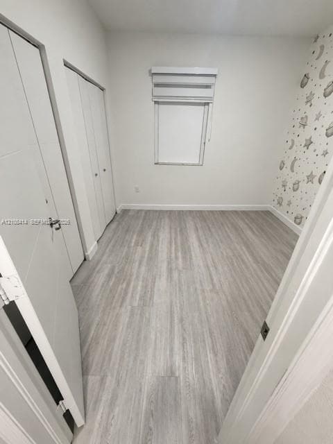 Room featuring wood-finish flooring, dual-panel closet doors, and a window with a mounted roller shade