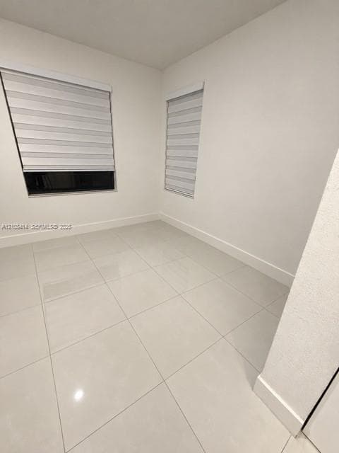 Neutral interior space featuring polished tile flooring, crisp white walls, and dual windows equipped with modern zebra-style roller shades