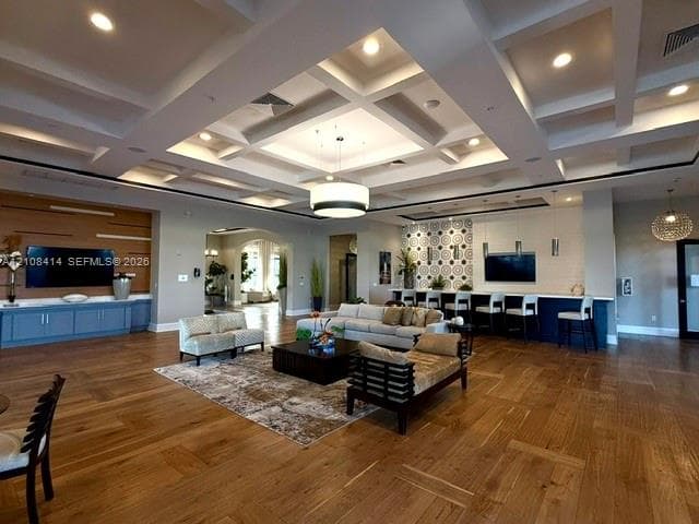 Coffered ceiling with integrated recessed lighting, wood-finish flooring, built-in cabinetry with wall-mounted television, and a service bar featuring pendant lighting