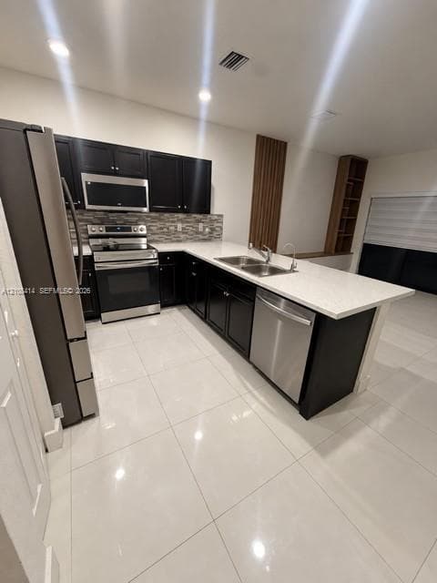Kitchen featuring dark cabinetry, stone-finish countertops, stainless steel appliances, a multi-tone tile backsplash, and oversized light-colored floor tiling
