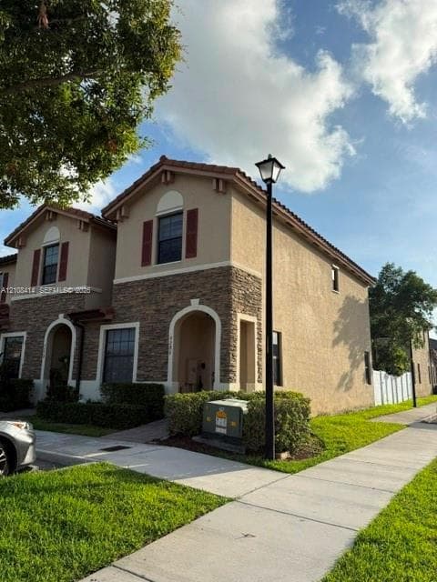 Two-story exterior featuring a stucco facade, stone veneer accents, arched entryway, and louvered shutters