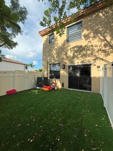 Rear exterior featuring a two-story stucco facade, synthetic turf lawn, white vinyl privacy fencing, and sliding glass patio doors