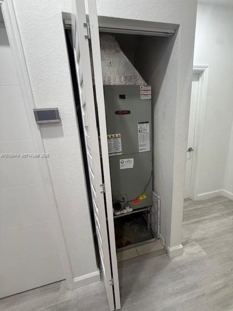 Dedicated mechanical closet featuring a climate control unit with louvered door access and wood-finish flooring