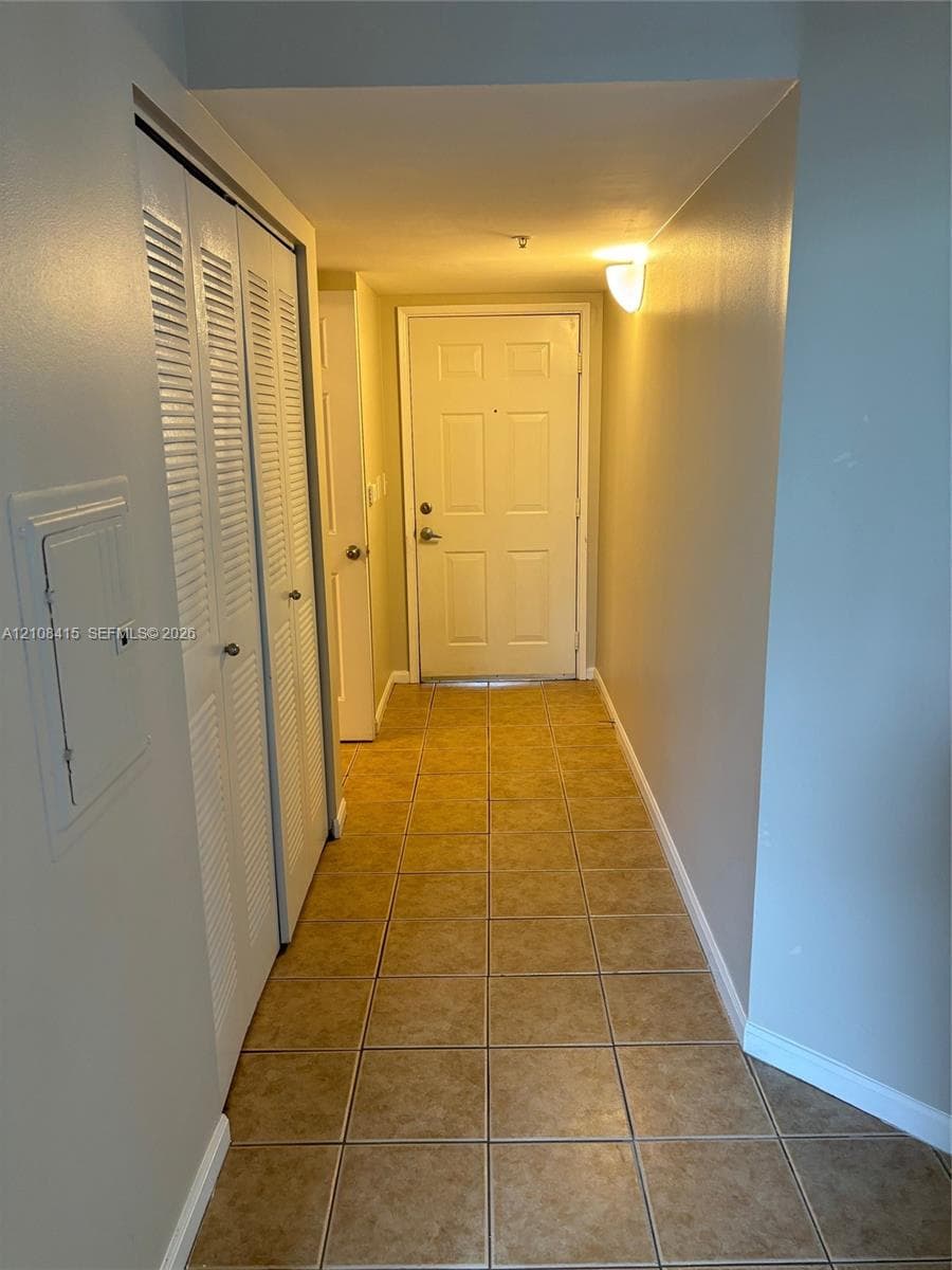 Interior hallway featuring tile flooring, louvered-style closet doors, and wall-mounted lighting