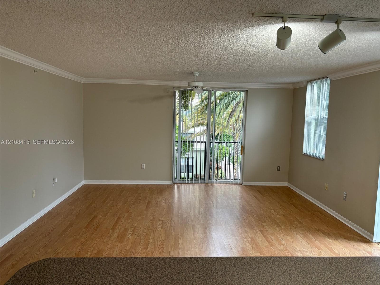 Living area featuring wood-finish flooring, crown molding, sliding glass door with balcony access, ceiling fan, and adjustable track lighting