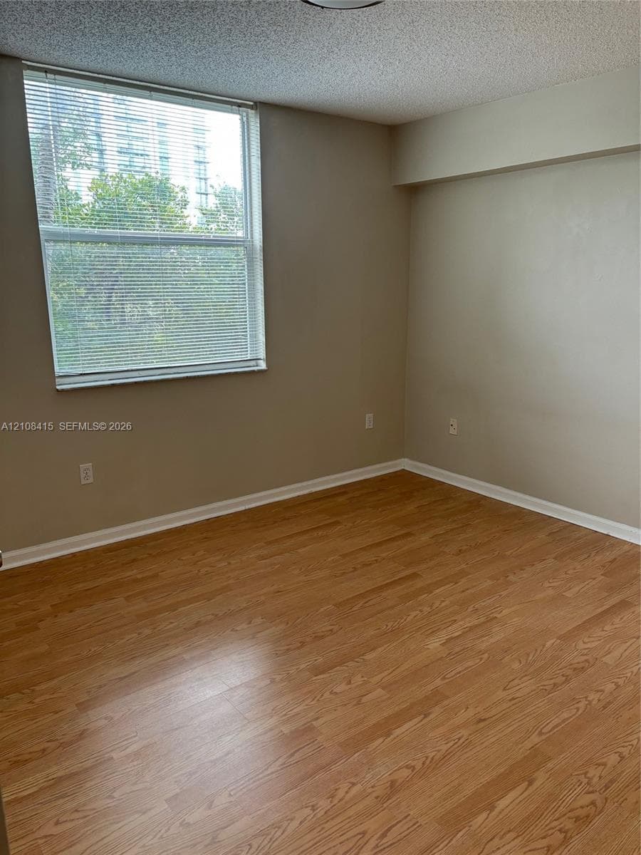 Room featuring wood-finish flooring, neutral wall paint, and a large window with horizontal blinds