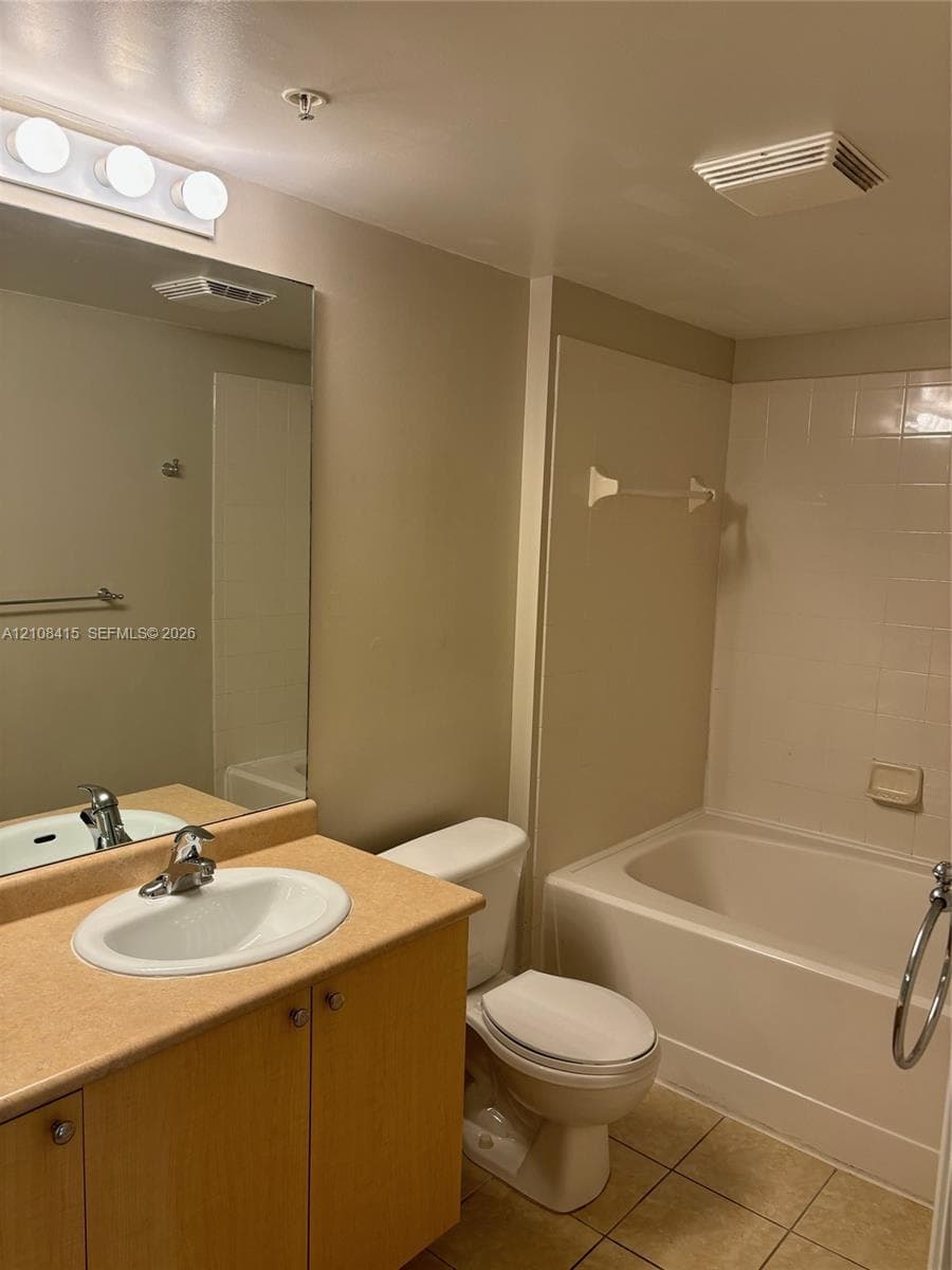Bathroom featuring a vanity with a solid-surface countertop, an integrated oval basin, light wood-finish cabinetry, a large wall-mounted mirror, and a tiled tub-shower combination