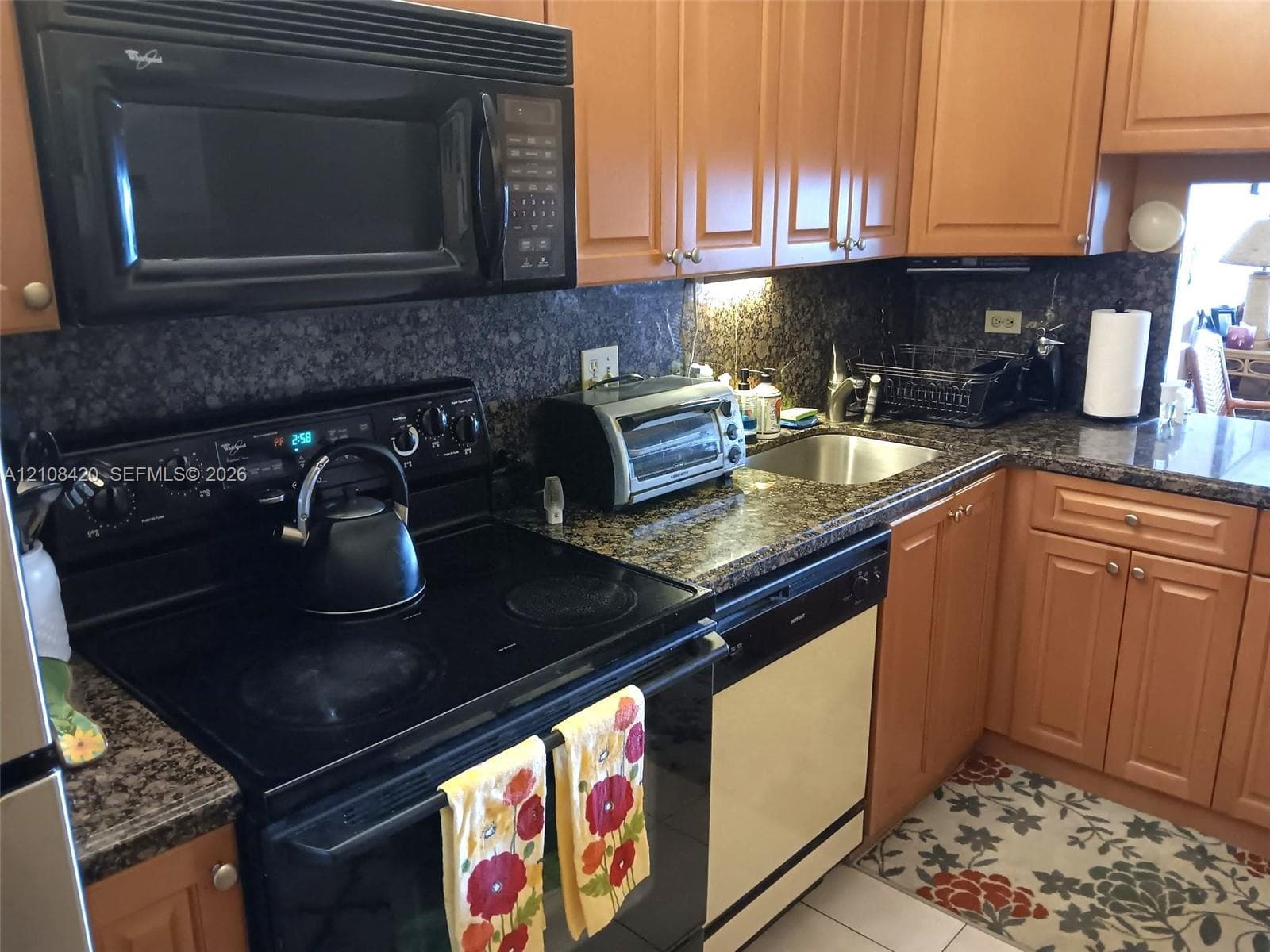 Kitchen featuring medium-tone wood cabinetry, dark stone countertops, an integrated over-the-range microwave, a smooth-top electric range, and a stainless steel undermount sink
