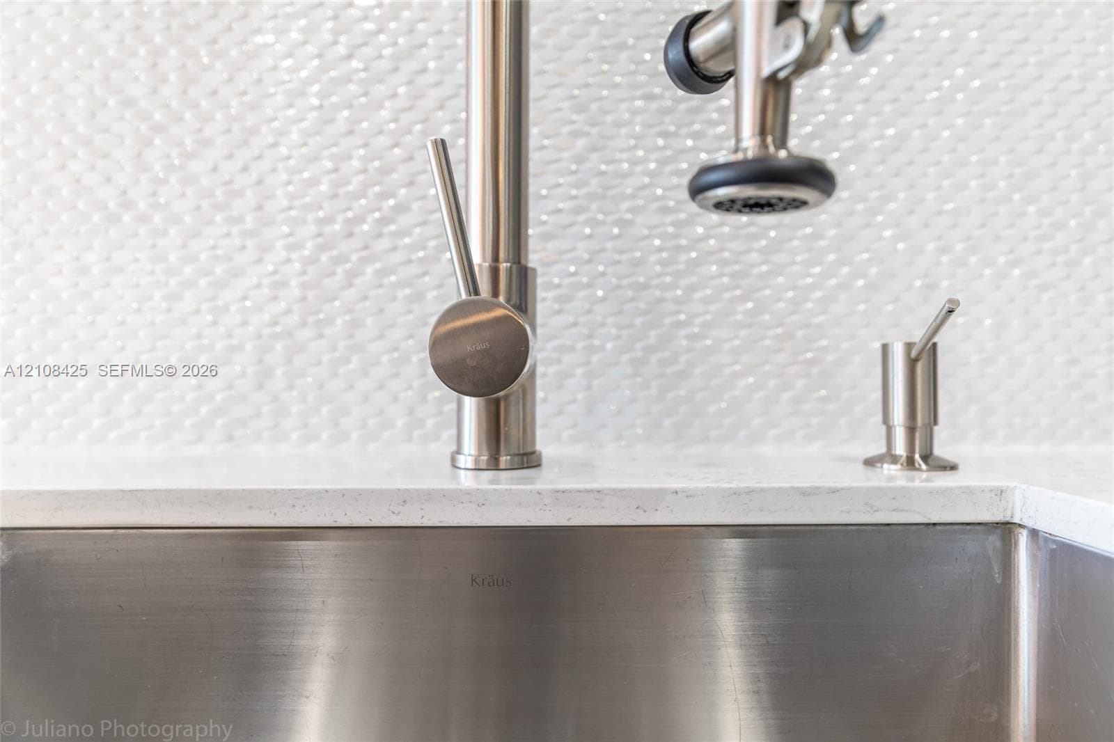 Brushed nickel commercial-style pull-down faucet, stainless steel undermount sink, solid surface countertop, and textured white tile backsplash