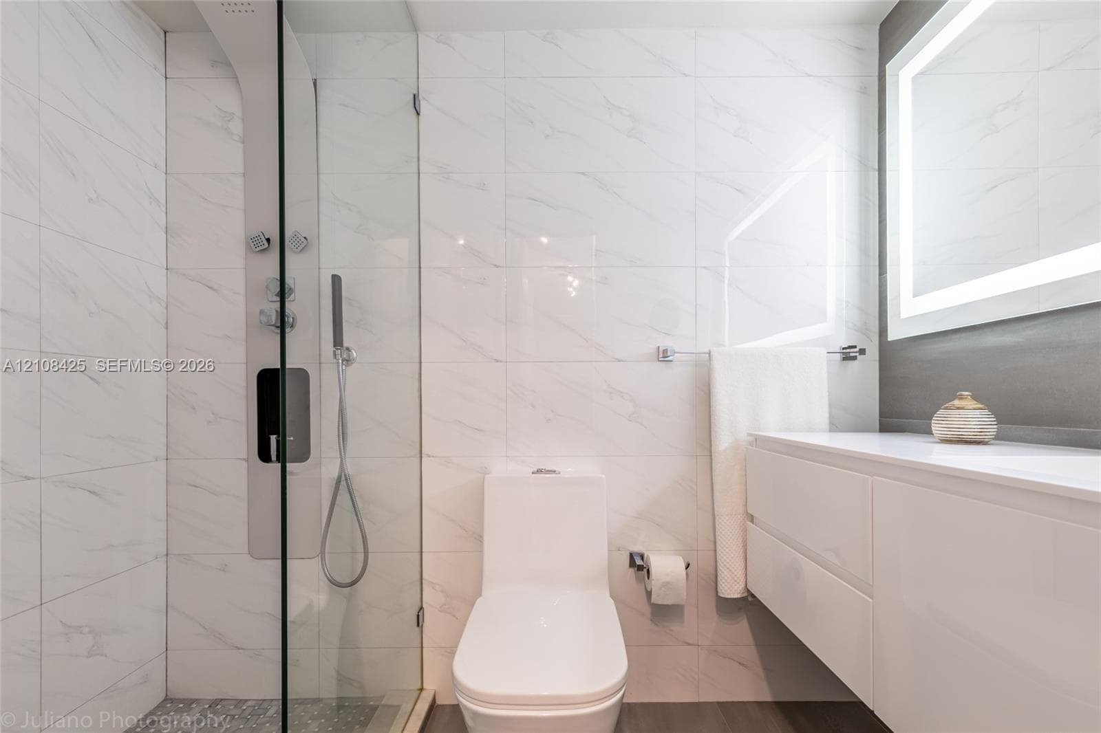 Shower enclosure featuring full-height tile surround, integrated multi-head shower system, floating dual-drawer vanity, and wall-mounted LED-backlit mirror
