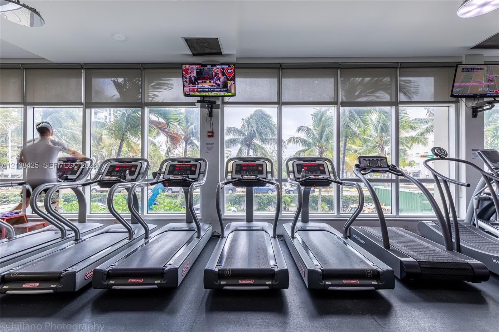 Fitness center featuring floor-to-ceiling windows with roller shades, recessed lighting, and integrated wall-mounted televisions