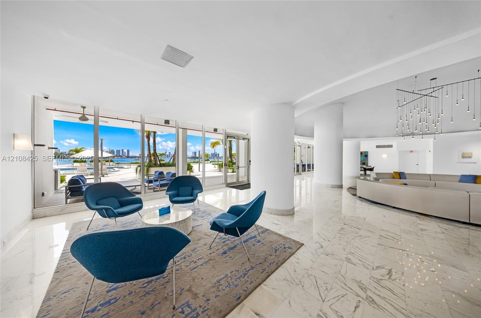 Open-concept space featuring polished stone flooring, floor-to-ceiling glass walls, prominent structural columns, and a multi-tiered modern chandelier
