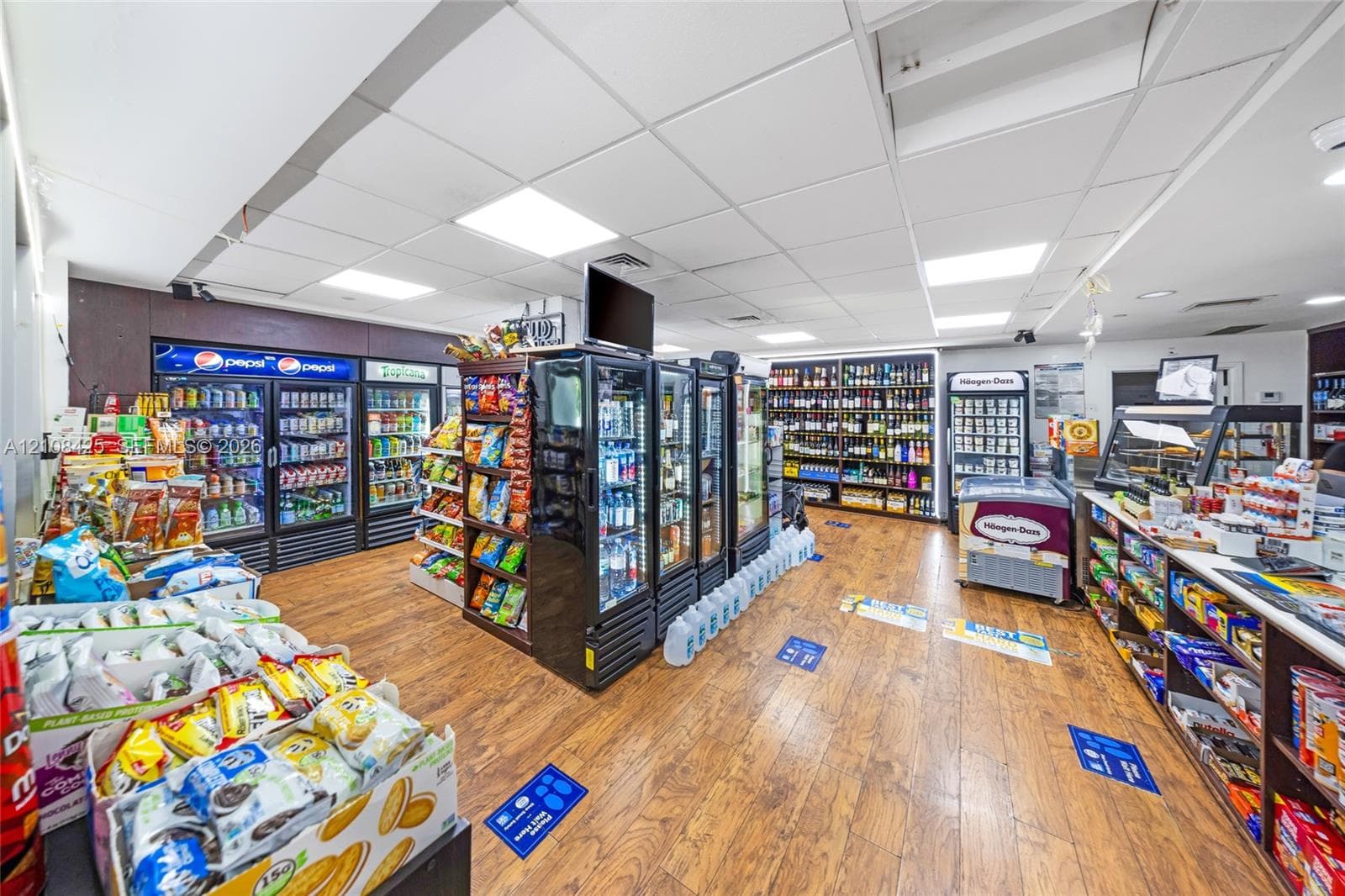 Commercial interior featuring wood-finish flooring, extensive built-in shelving, multiple glass-door refrigeration units, and drop-ceiling lighting