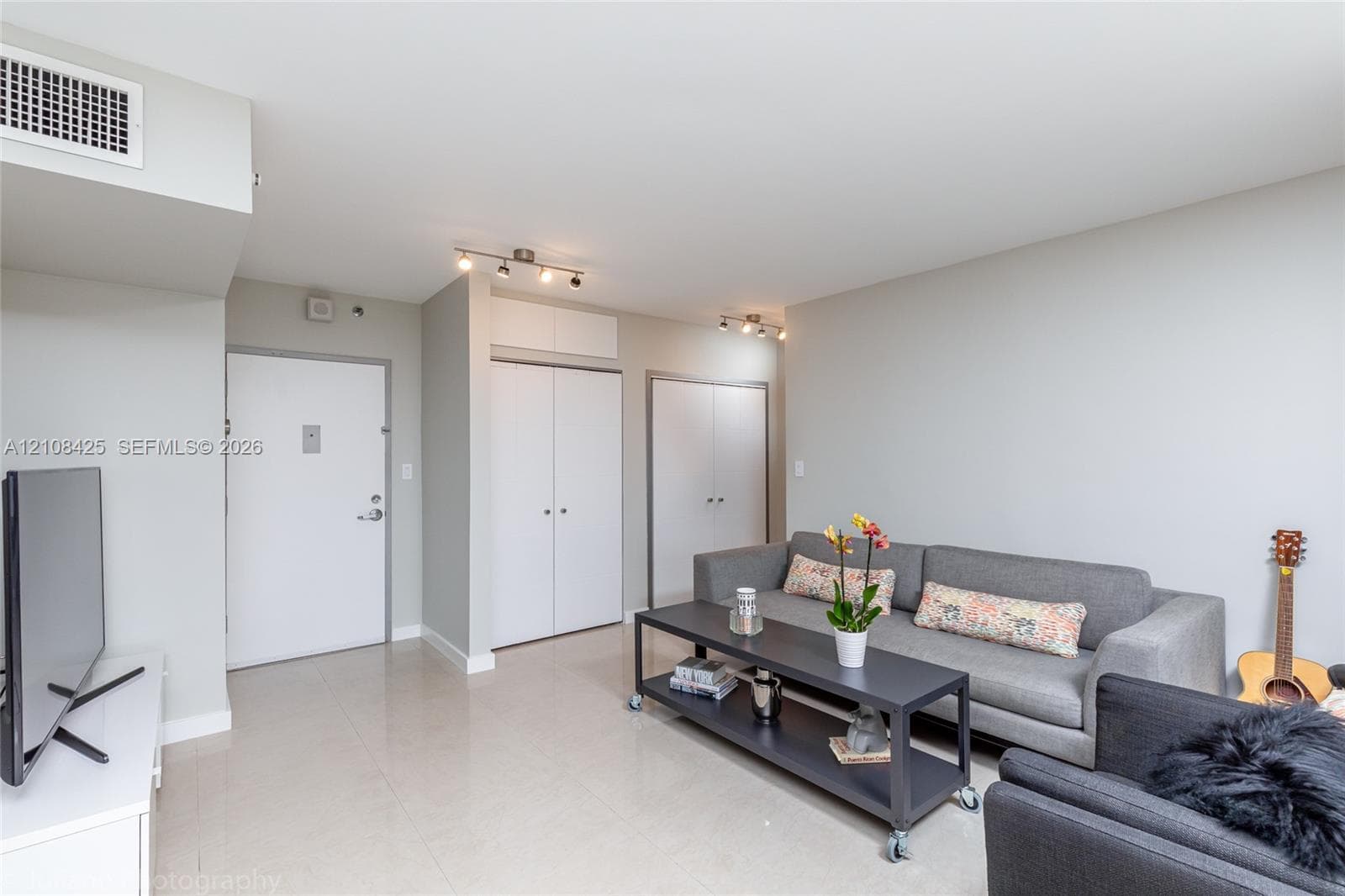 Interior space featuring polished tile flooring, neutral wall tones, multi-unit closet storage with overhead compartments, and adjustable multi-directional track lighting