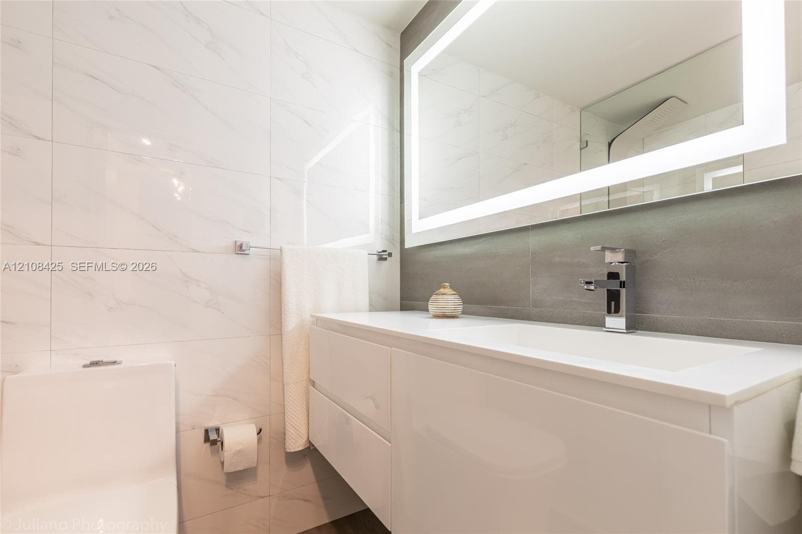 Modern floating vanity with a seamless countertop, integrated rectangular sink, wall-mounted faucet, oversized LED-backlit mirror, and full-height stone-finish wall tile