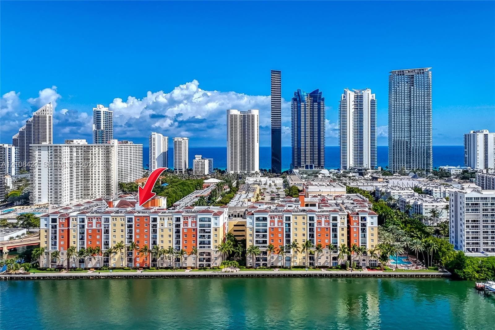 Multi-story residential complex featuring waterfront positioning, private balconies, tile roofing, and mature palm landscaping