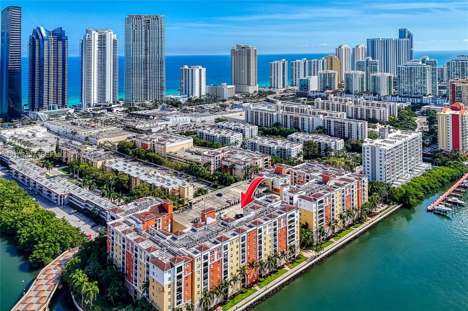 Aerial view of a multi-story waterfront residential complex featuring a red-tiled roof, exterior stucco facade, and an integrated parking structure