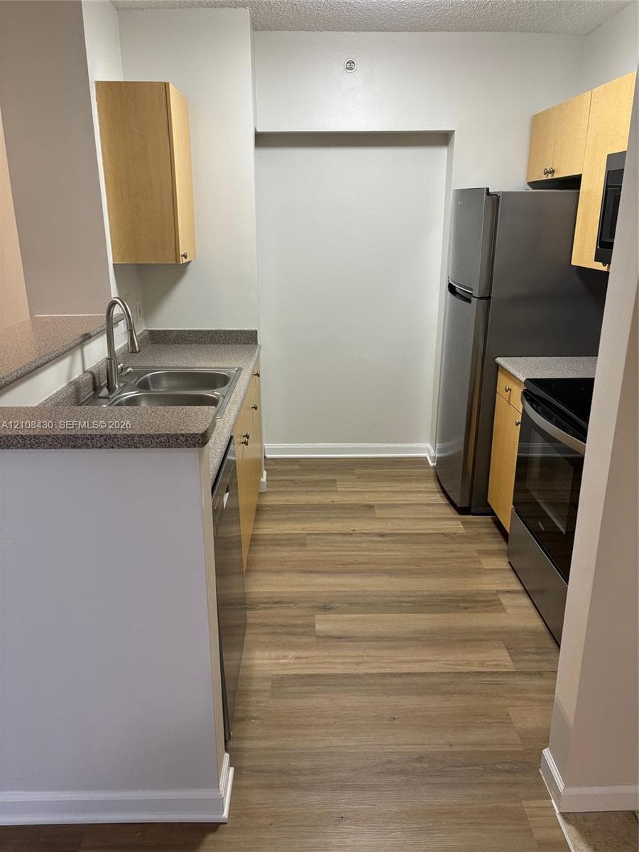 Kitchen featuring wood-finish cabinetry, stone-texture countertops, stainless steel appliances, wood-finish flooring, and a dual-basin sink with a pull-down faucet