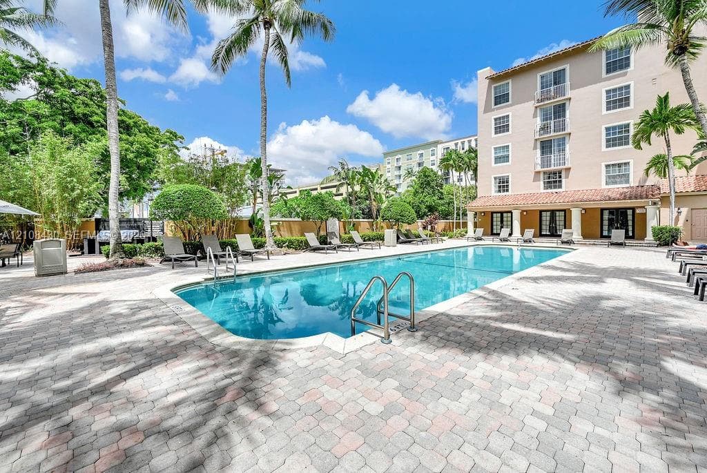 In-ground swimming pool with a stone paver deck, perimeter landscaping, and mature palm trees