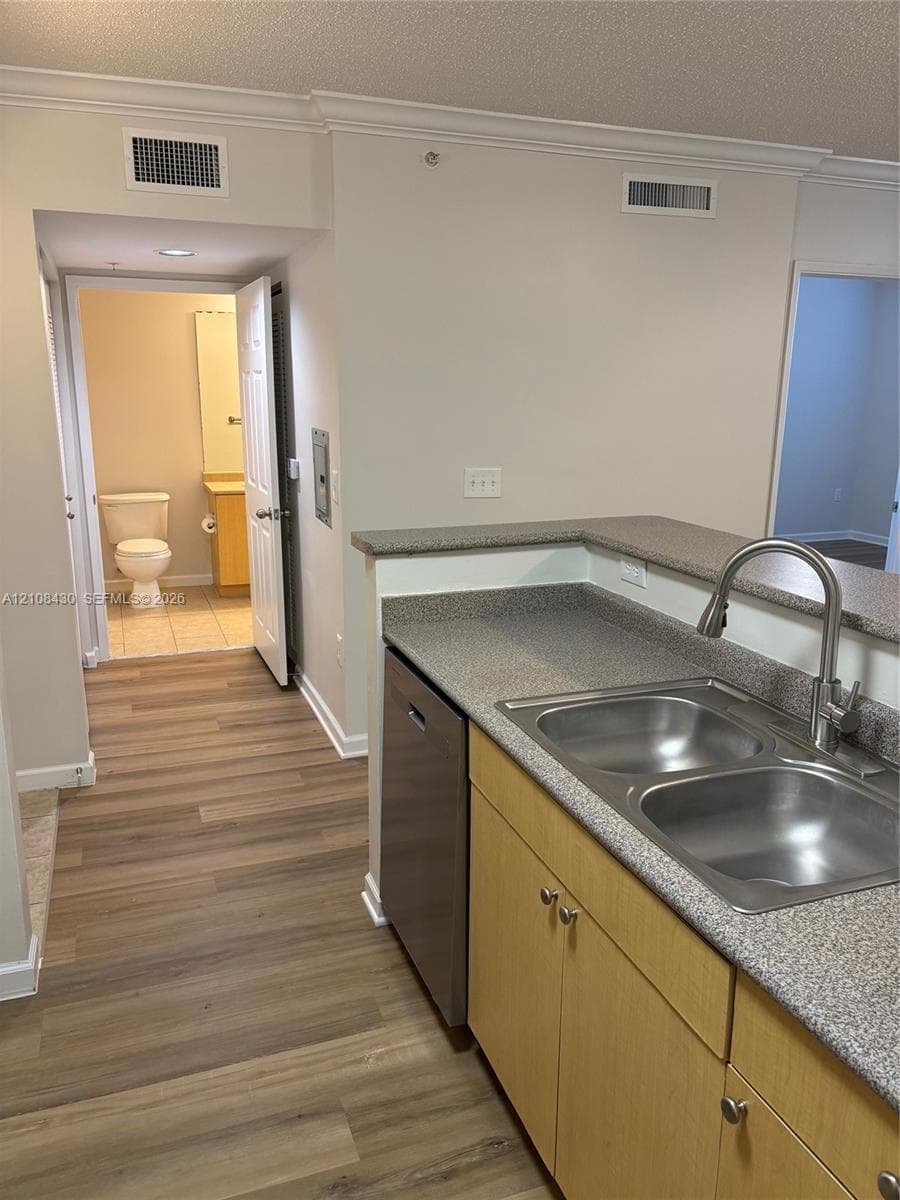 Kitchen featuring a dual-basin stainless steel sink, gooseneck faucet, integrated dishwasher, solid-surface countertops, and wood-finish flooring