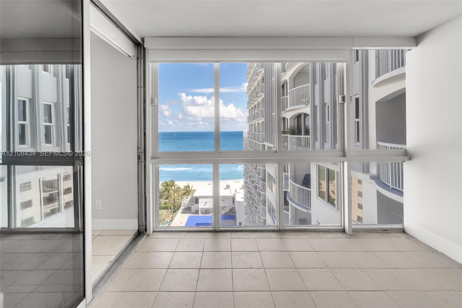 Enclosed balcony featuring tile flooring, floor-to-ceiling windows, and sliding glass panel doors, showcasing ocean and coastline scenery