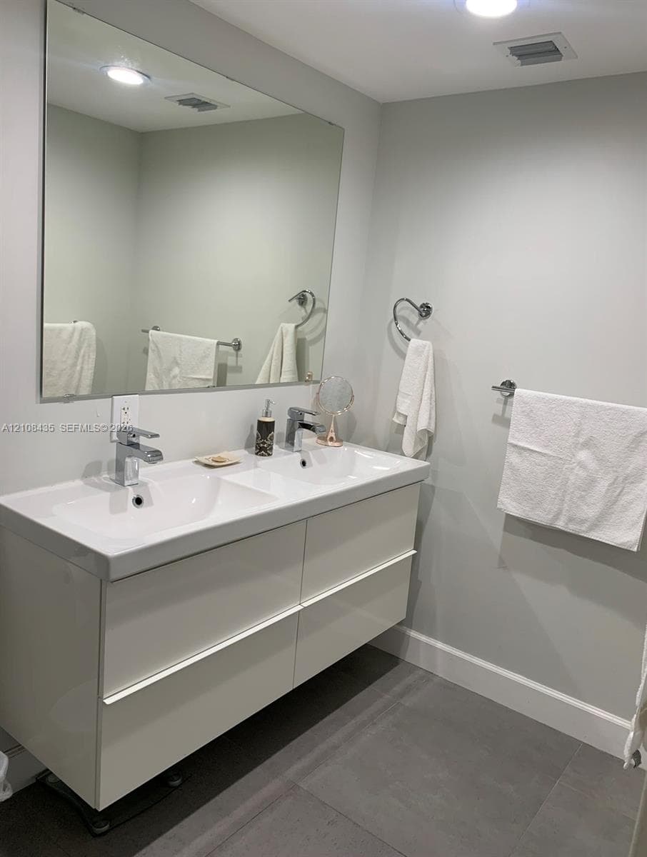 Floating double vanity with integrated dual sinks, polished chrome faucets, large wall-mounted mirror, and tile flooring