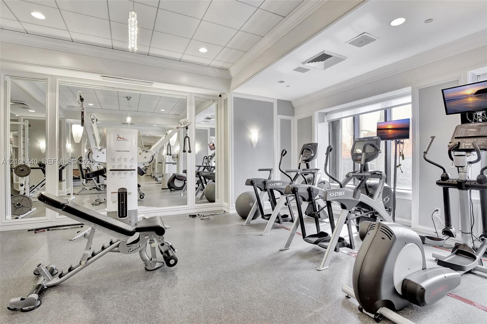 Fitness space featuring floor-to-ceiling mirrors, a coffered ceiling with recessed lighting, wall-mounted sconces, and impact-resistant rubber flooring
