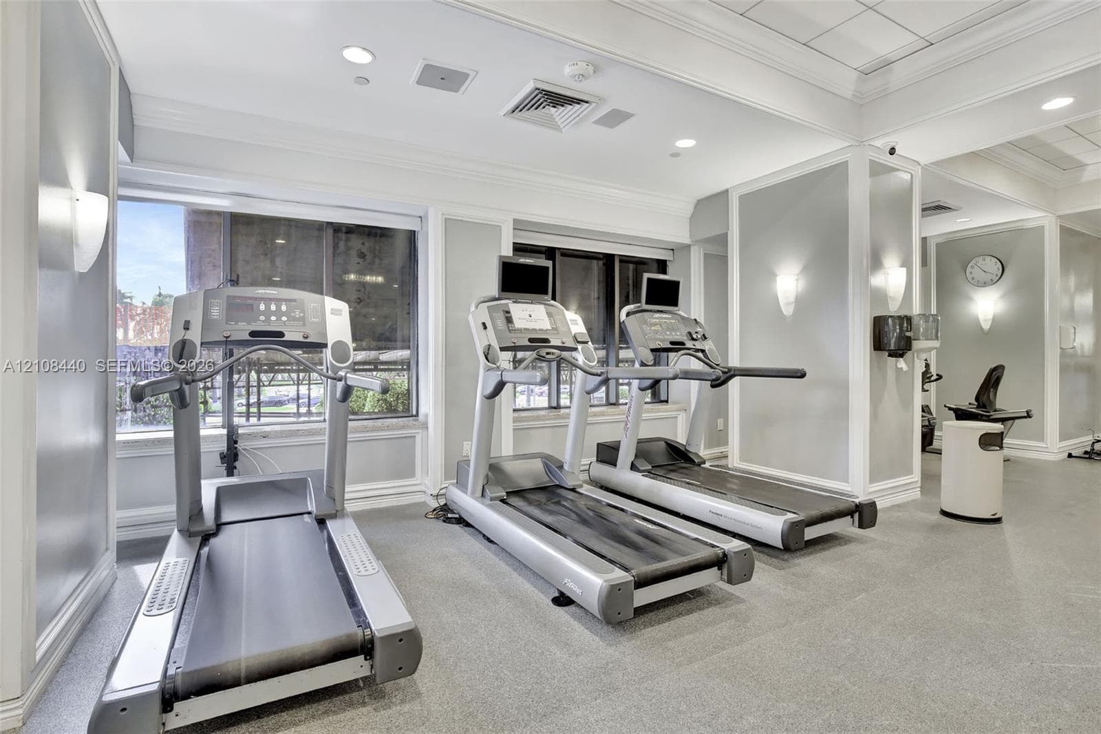 Fitness center featuring large windows, recessed ceiling lighting, wall-mounted sconces, and crown molding