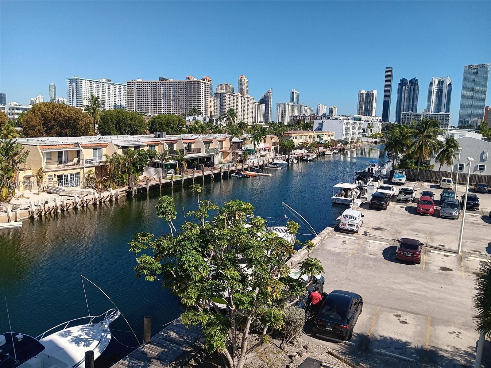 Waterfront setting featuring a concrete bulkhead, private boat slips, paved parking area, and mature palm trees
