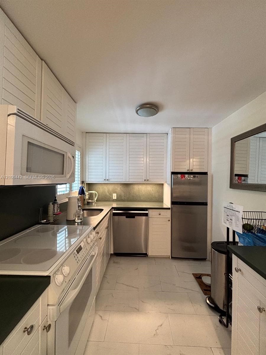 Kitchen featuring white louvered cabinetry, stainless steel appliances, dark countertops, and light-toned tile flooring