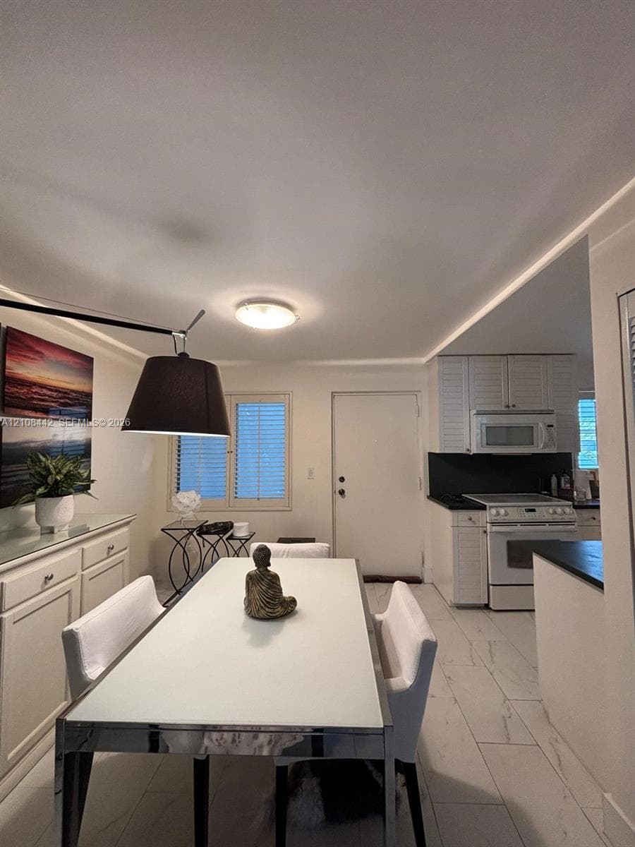 Kitchen and dining area featuring stone-look tile flooring, white cabinetry with louvered-style doors, matte black countertops, and a built-in over-the-range microwave