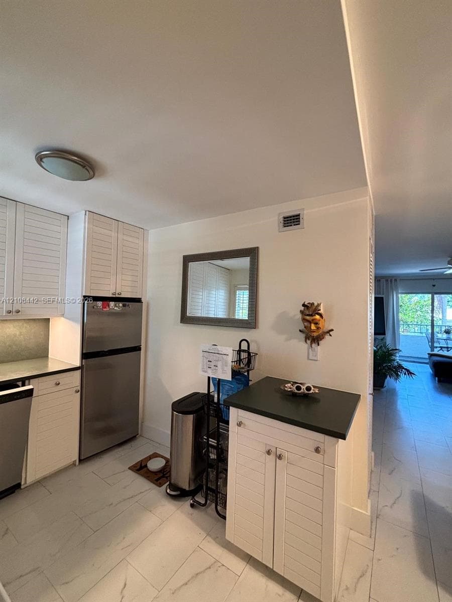 Kitchen featuring white louvered cabinetry, stainless steel refrigerator, stone-finish countertops, and large-format tile flooring