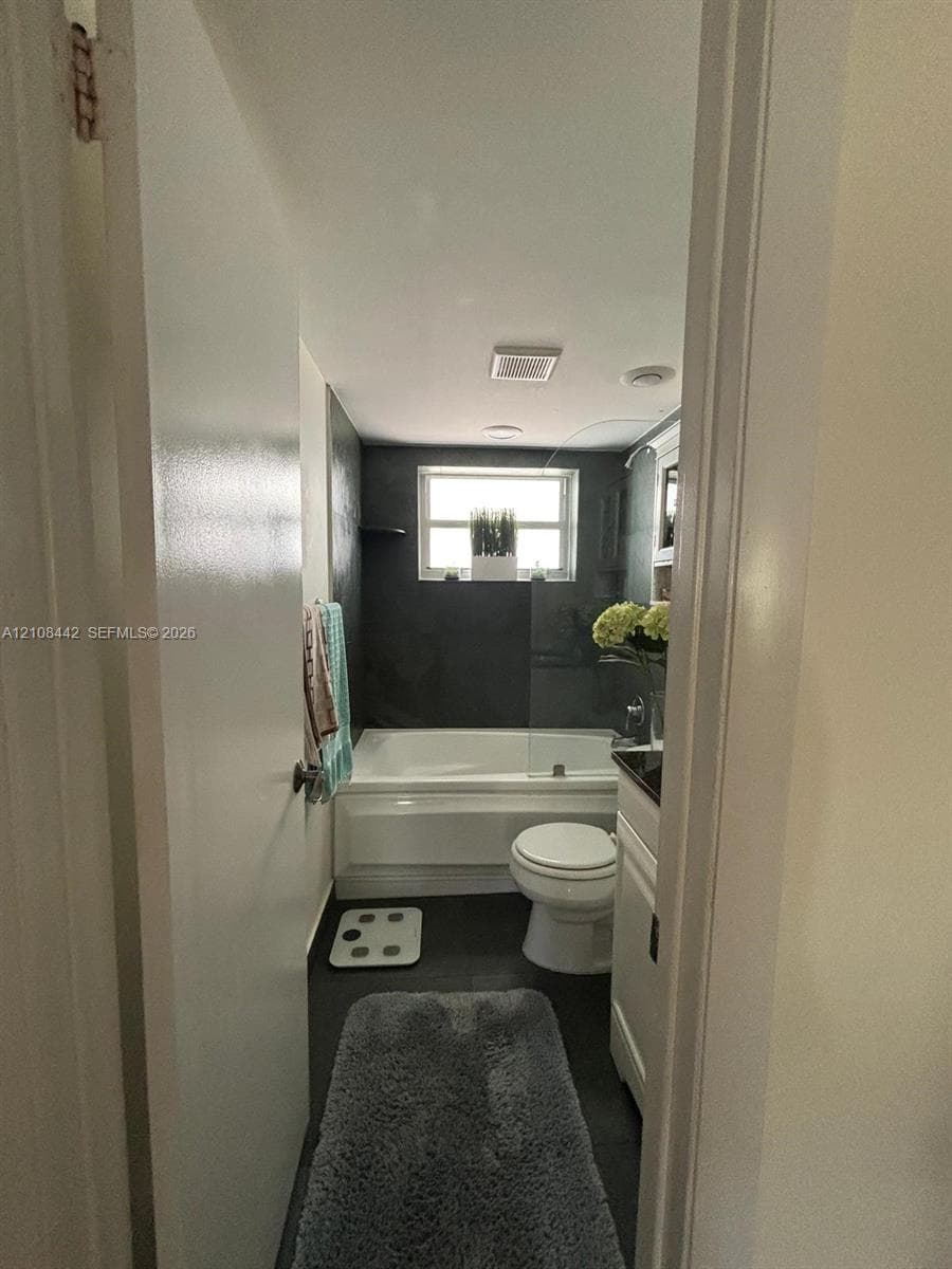 Bathroom featuring a deep soaking tub, dark tiled walls, glass shower panel, and white vanity cabinetry with a dark countertop