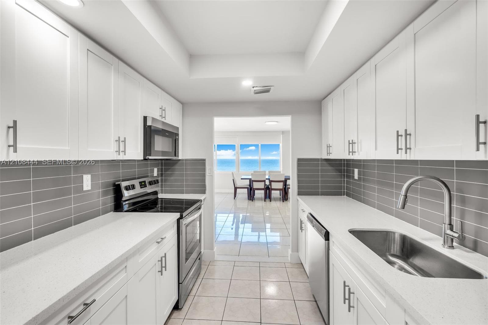 Kitchen featuring white shaker-style cabinetry, solid-surface countertops, horizontal gray tile backsplash, stainless steel appliances, and large-format tile flooring