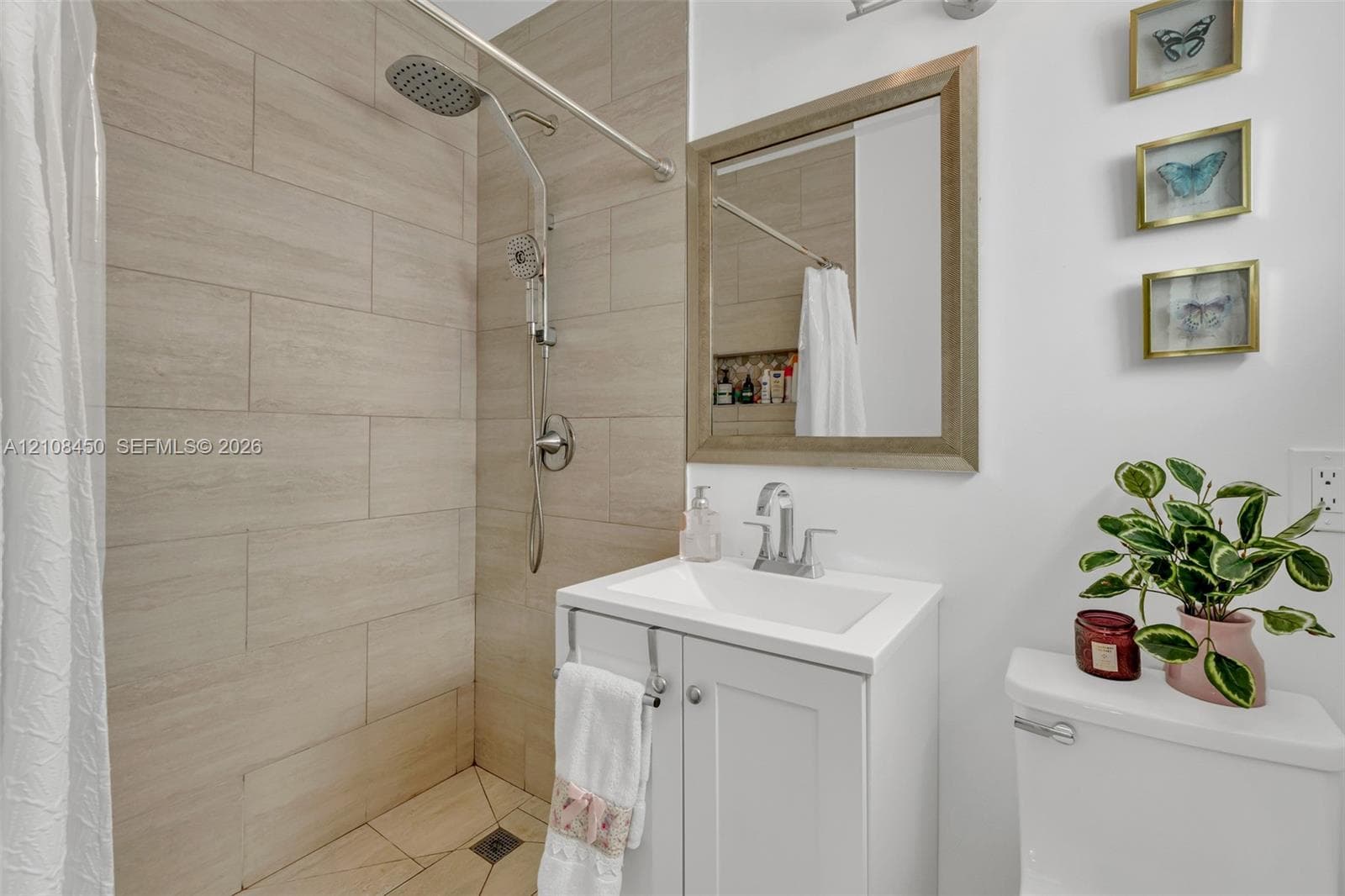 Bathroom featuring large-format neutral wall tile, rain-style showerhead, white vanity cabinet with a rectangular basin, and a framed mirror