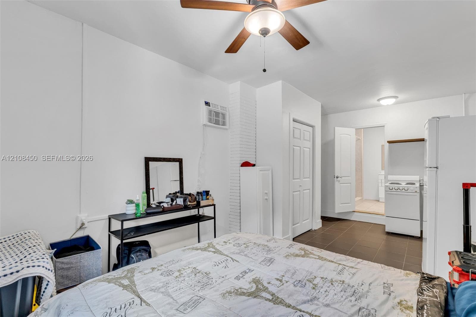 Room featuring white walls, a ceiling fan with integrated lighting, dark tile flooring, a wall-mounted cooling unit, and a built-in pantry