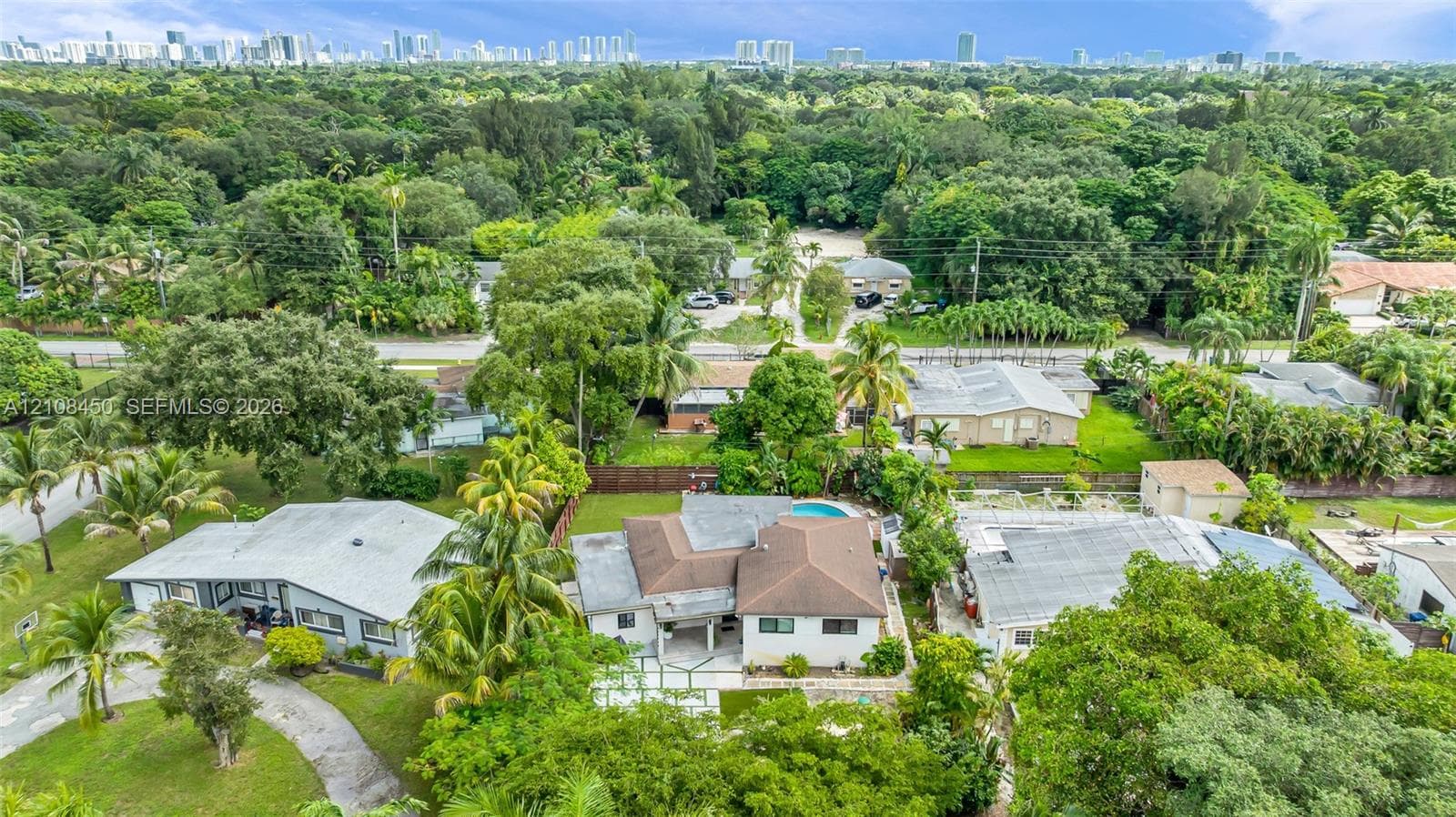 Aerial perspective featuring a multi-hipped roofline, paved driveway, swimming pool, and dense mature landscaping