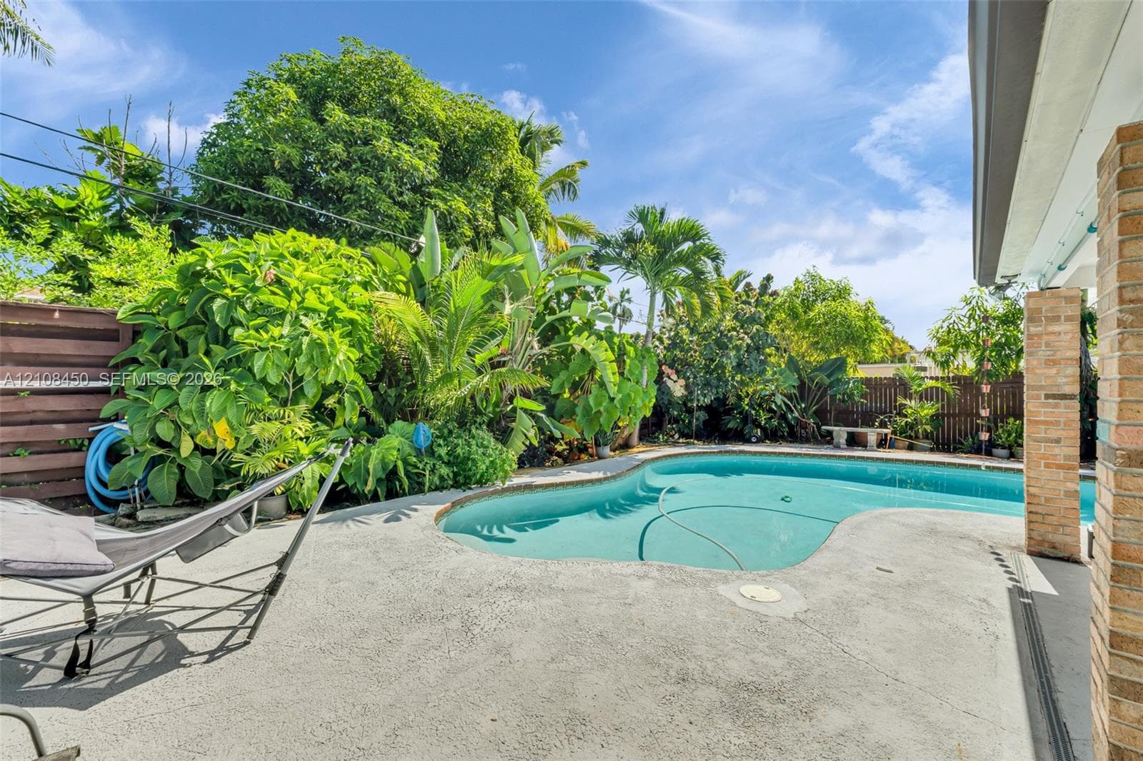 Outdoor swimming pool with curved concrete decking, horizontal slat wood fencing, and mature tropical landscaping