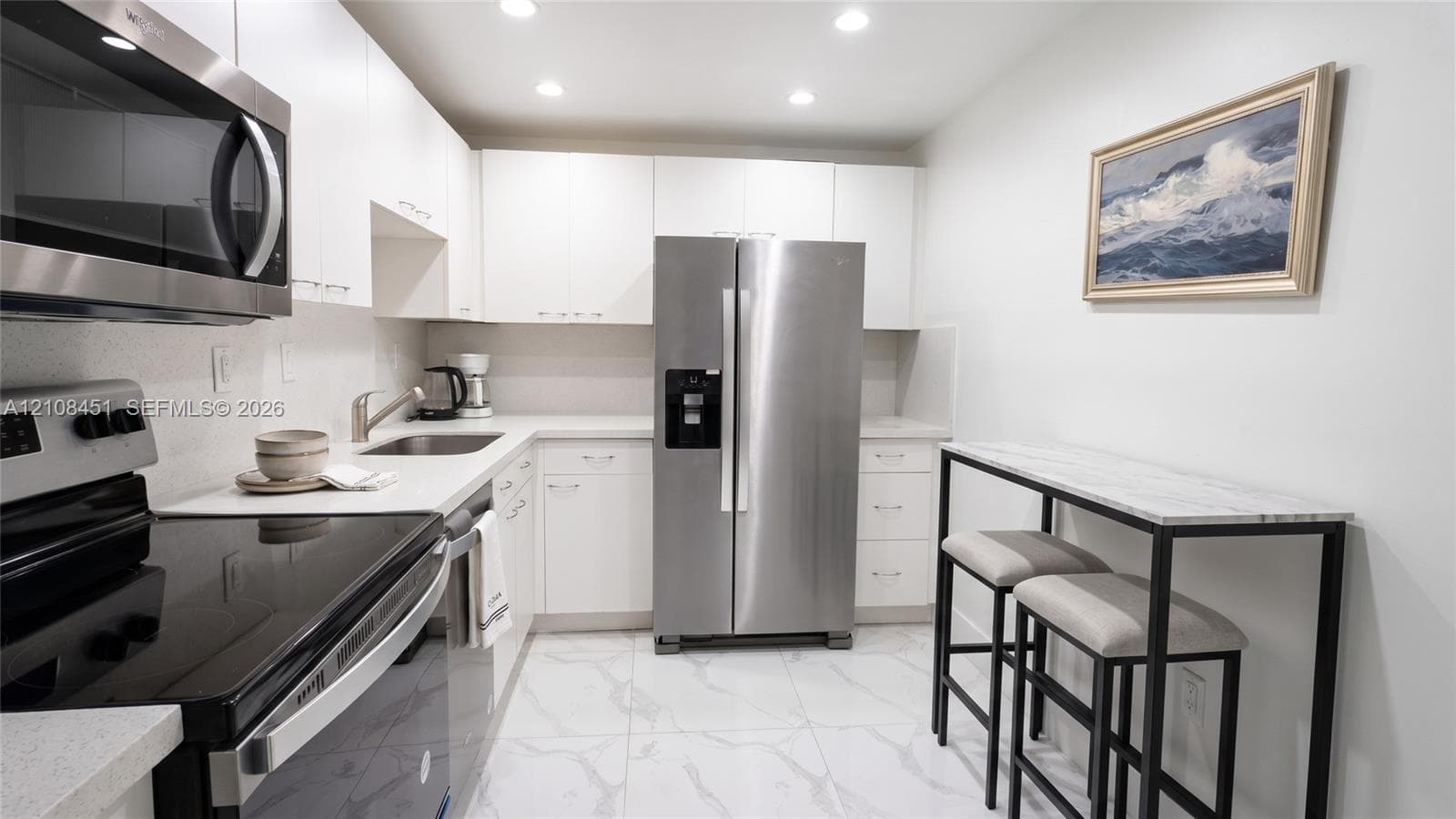 Kitchen featuring white flat-panel cabinetry, stainless steel appliances, solid surface countertops, and white tile flooring with grey veining