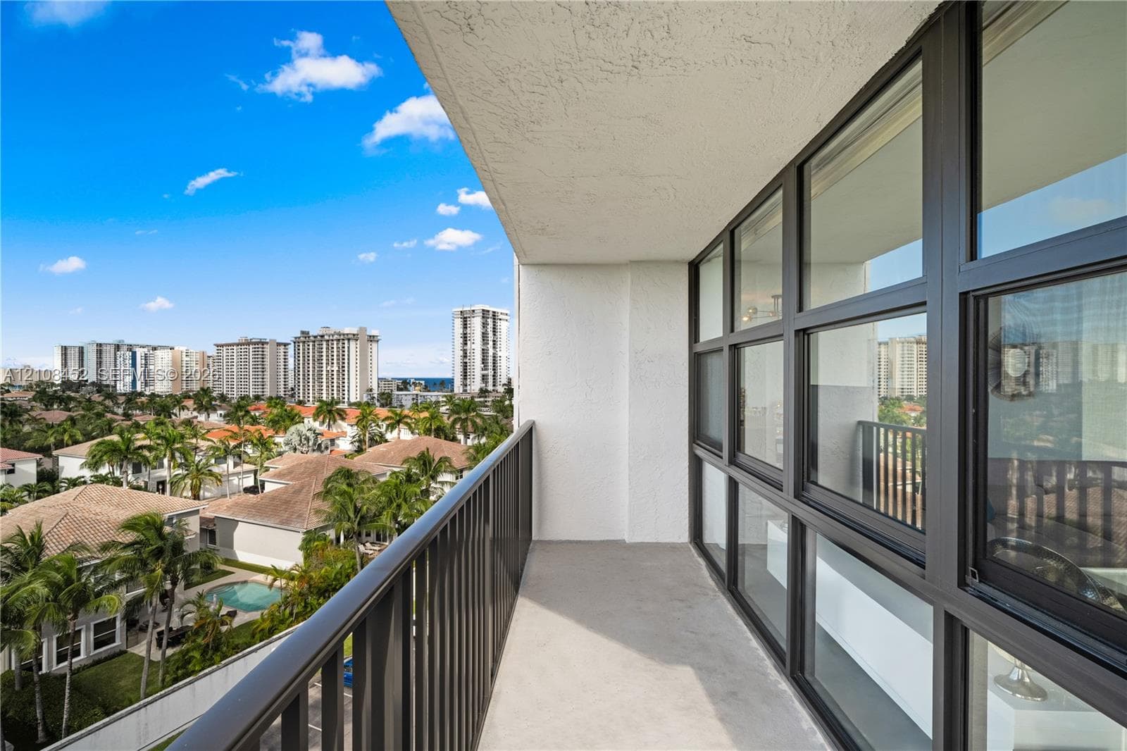 Covered balcony featuring metal railing, concrete flooring, and extensive glass window wall with dark framing