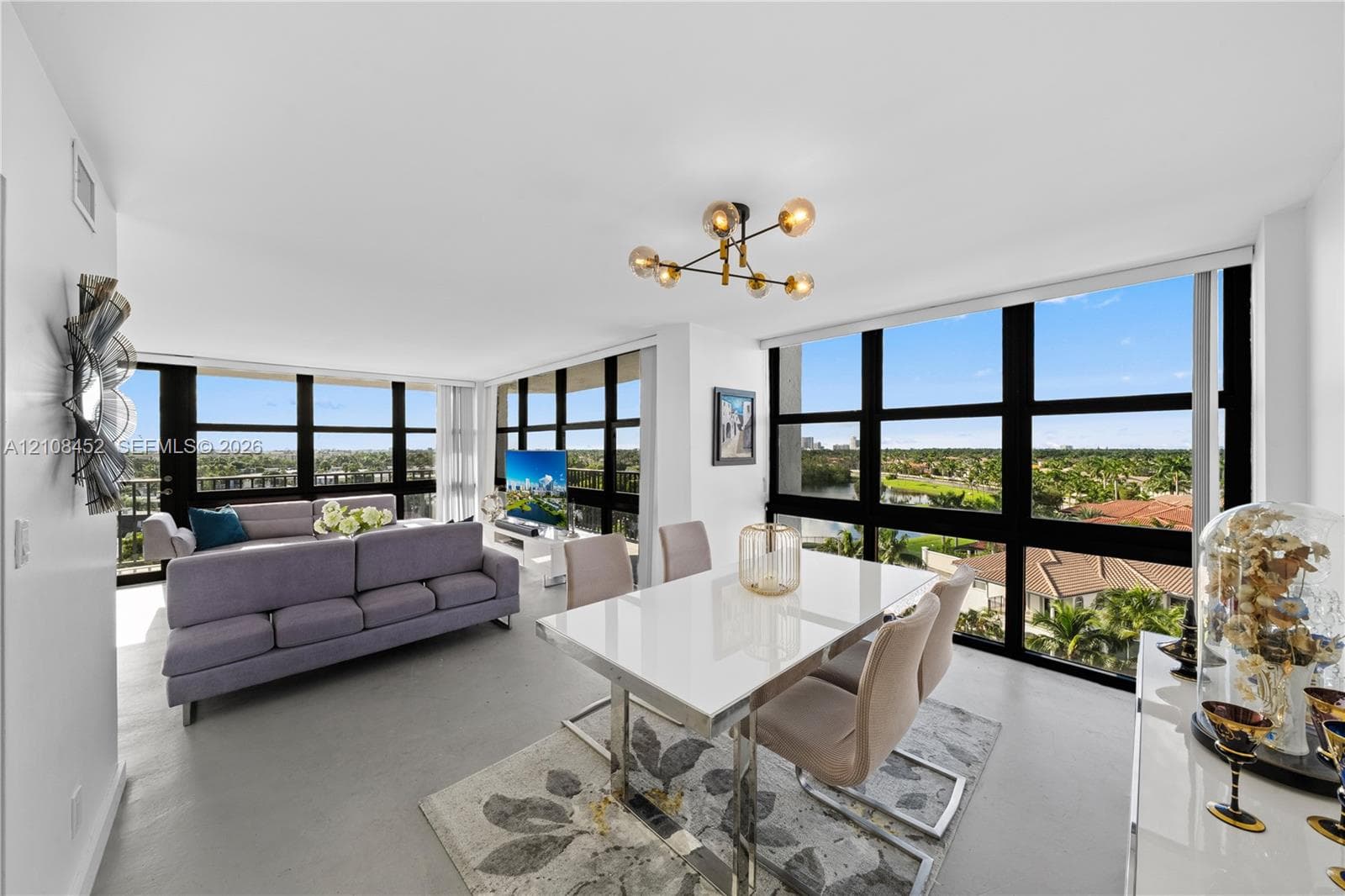 Open-concept living space featuring floor-to-ceiling windows, uniform light-toned flooring, and a multi-arm geometric ceiling fixture